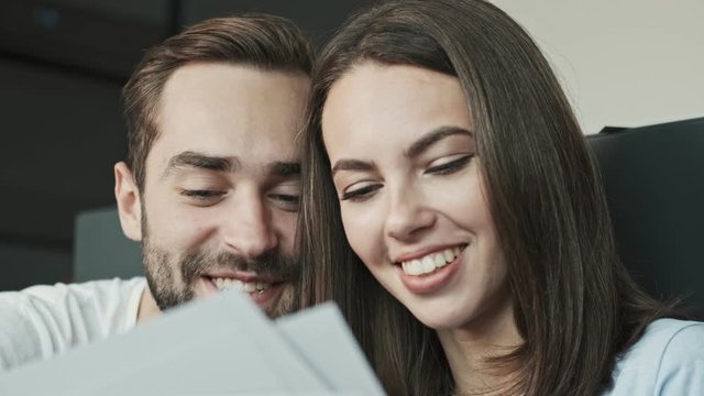 Cropped view of charming happy young lovely couple looking at family portraits and smiling while sitting at home