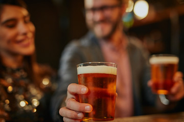 Man standing in group and giving beer to a friend. Irish pub interior. Nightlife.