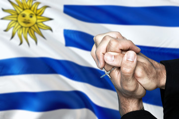 Uruguay flag and praying patriot man with crossed hands. Holding cross, hoping and wishing.