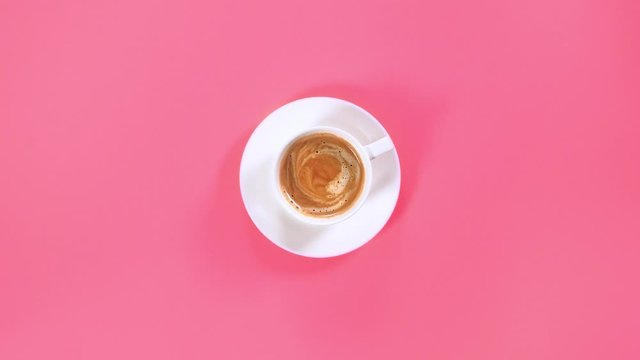 Top view. Female hand puts a cup of black coffee on the table, pink background