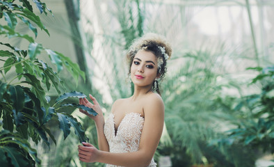 Happy tanned bride in beautiful white dress posing in spring park