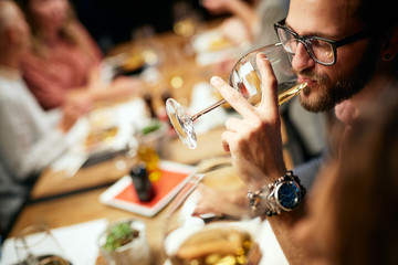 Handsome caucasian bearded hipster man with eyeglasses drinking wine while sitting with his friends...