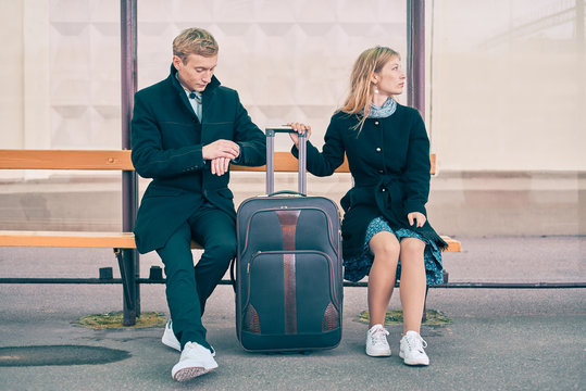 man and woman at a bus stop waiting for transport. the guy looks at the clock