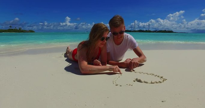 summer romance concept. young lovely couple drawing heart in the white soft sand on the tropical beach. Caribbean