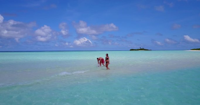 Romantic couple walking in the water on high tide, sandbank with white sand . distant island and bright blue sky with white clouds