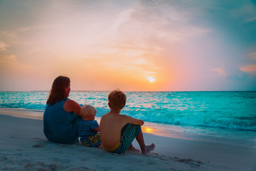 mother with son and daughter looking at sunset on beach