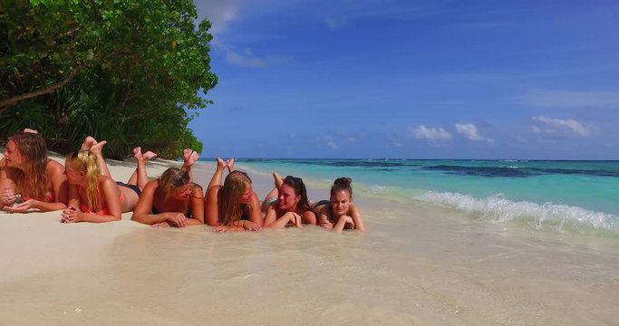 Happy girls on their vacation days lying on white sandy beach washed by sea waves on a lush vegetation island in Jamaica
