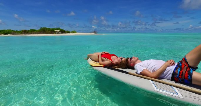 Cute couple lying on surf board waved by crystal emerald sea water near paradise exotic island in Malaysia