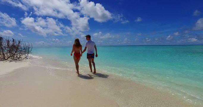 Happy young couple walking around white tropical beach, seeking for seashells hidden on fine sand of Jamaica