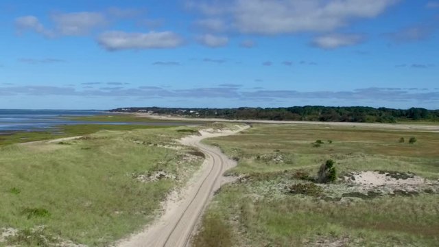 Peaceful drone footage of an idyllic dune road along a breathtaking New England beach on Cape Cod in the summer.