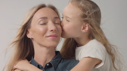 Daughter kiss her mother to cheek and both with eyes closed. Closeup family portrait of mother and daughter showing her love