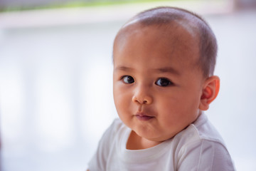 A cute Asian male baby wearing a white shirt, about six months old is smiling on a white background.