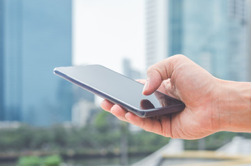 close up handsome man using hand typing smartphones and touch screen working search with app devices outdoor in city with sunrise and building background. 5G technology connecting the world.