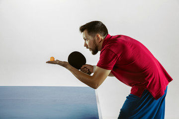 Young man plays table tennis on white studio background. Model in sportwear plays ping pong....