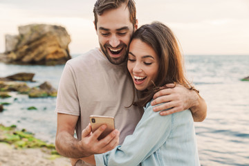 Photo of excited young couple using cellphone and hugging