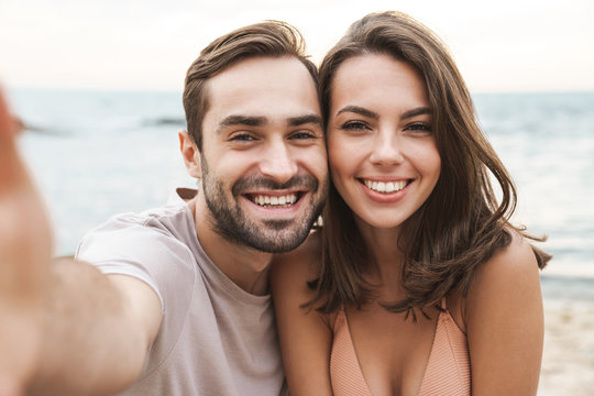 Photo of joyful young couple smiling and taking selfie photo