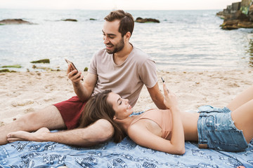 Photo of cheerful young couple using cellphones and smiling