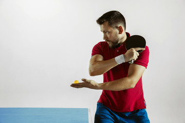 Young man plays table tennis on white studio background. Model in sportwear plays ping pong....