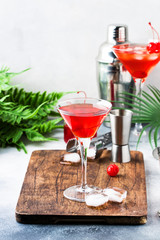 Cosmopolitan cocktail with vodka, liqueur, cranberry juice, lime, ice and orange zest, gray bar counter background, bartender tools, copy space