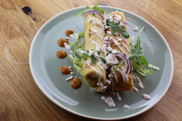 Delicious chicken burrito with salad, cheese, mayonnaise and ketchup on a white plate.
