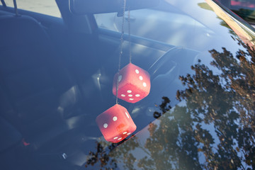 Fuzzy dice hanging on the rearview mirror in a car for good luck. - obrazy, fototapety, plakaty