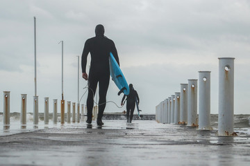 Surfing as a lifestyle. Surfers putting on wetsuits go along the city pier to the sea. Concept:...