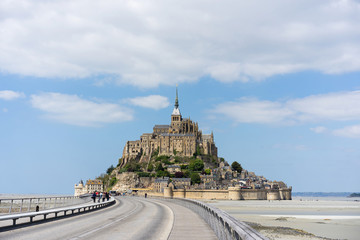 Fototapeta na wymiar Distant view of Mont Saint Michel in low tide west France with clouds in the blue sky