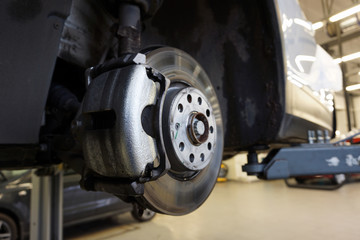 Front brake of a modern car. The front brake caliper is in focus, and the service station is blurry in the background. 