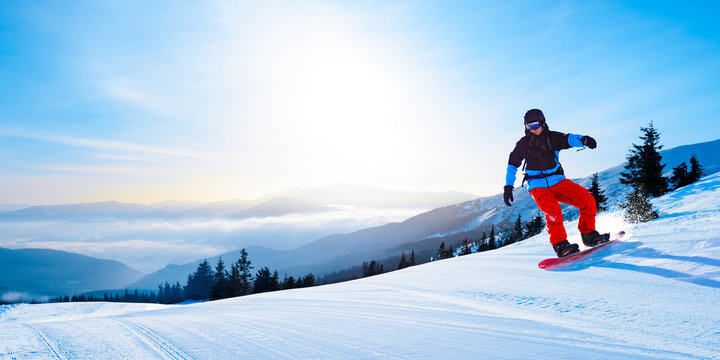 Snowboarder Riding Red Snowboard in Mountains at Sunny Day. Snowboarding and Winter Sports