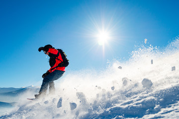Naklejka na ściany i meble Snowboarder Riding Red Snowboard in Mountains at Sunny Day. Snowboarding and Winter Sports