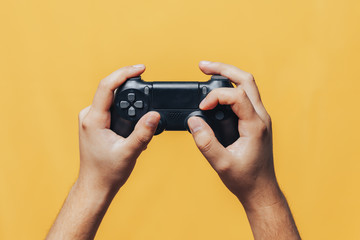 man gamer hands holding black gamepad on yellow background.