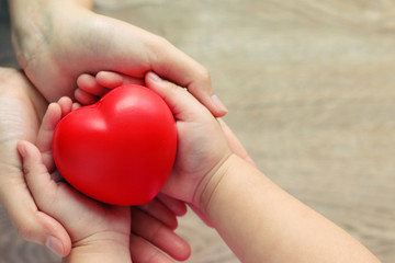 soft focus of Mom and Baby Holding Red Heart on Table. It expresses love, concern ,care and family