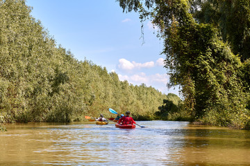 People (friends) kayaking in wild Danube river and lake on biosphere reserve in spring. Concept for friendship, adventure, travel, action, lifestyle and kayaking