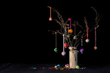 Christmas twig tree table decoration in rustic theme with colourful handmade baubles. Black background and glittery base with jungle bells and copy space.