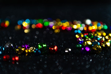 Multi-coloured Christmas jingle bells. Black blurred bokeh glitter background. Shallow depth of field. For overlay, background or texture.