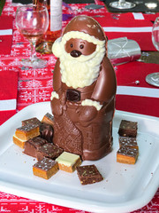 Chocolate Santa Claus with square chocolate treats on a red festive table on Christmas day.