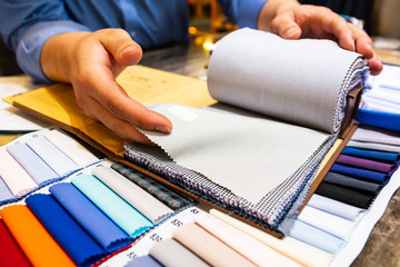 tailor choosing a fabric in swatch for his customer - obrazy, fototapety, plakaty
