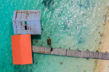 Top view of wooden jetty with clear sea water with young man taking selfie picture with drone at Mantanani Island, Sabah, Malaysia