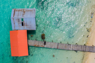 Top view of wooden jetty with clear sea water with young man taking selfie picture with drone at Mantanani Island, Sabah, Malaysia