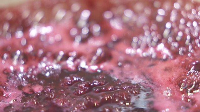 Process of making homemade raspberry jam. Red sweet syrup boiling on the stove closeup.
