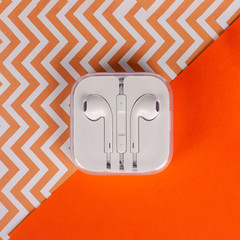 White mobile phone headphones in box on orange backgroind