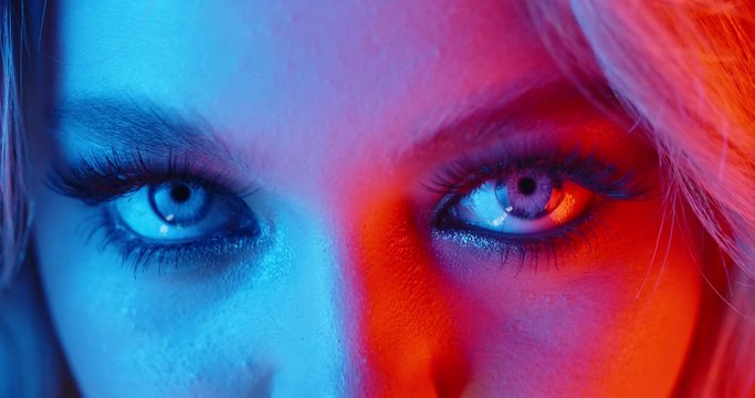 Sexy blonde girl with glowing makeup giving a seductive look in neon light - nightlife, nightclub concept 4k footage extreme close up shot