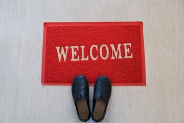 View of welcome carpet red color with black shoes on it.