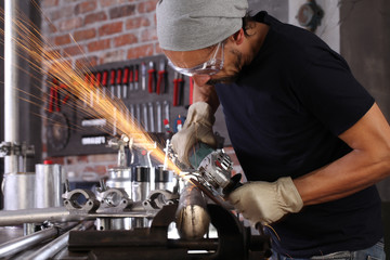 man work in home workshop garage with angle grinder, goggles and construction gloves, sanding metal makes sparks closeup, diy and craft concept