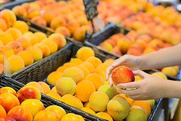 Female hand choosing peaches in the market.  Concept of information eating products, organic fruit and vegetables. 