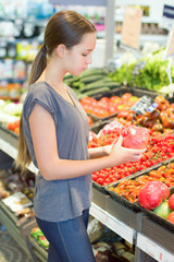 Teen girl shopping in supermarket, reading product information. Choosing daily product. Concept of healthy food, bio, vegetarian, diet.