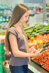 Teen girl shopping in supermarket, reading product information. Choosing daily product. Concept of healthy food, bio, vegetarian, diet.