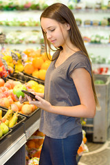 Teen girl shopping in supermarket, reading product information. Choosing daily product. Concept of healthy food, bio, vegetarian, diet.