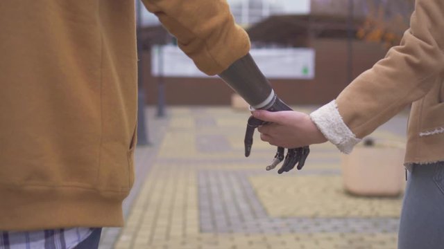 young man with a cyber prosthetic arm holds the hand of his beloved
