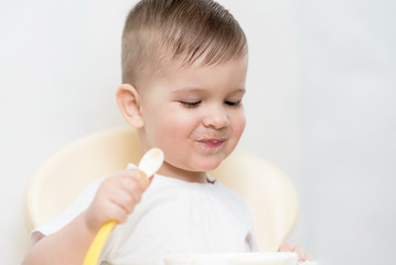 adorable baby boy eats porridge with a small spoon himself